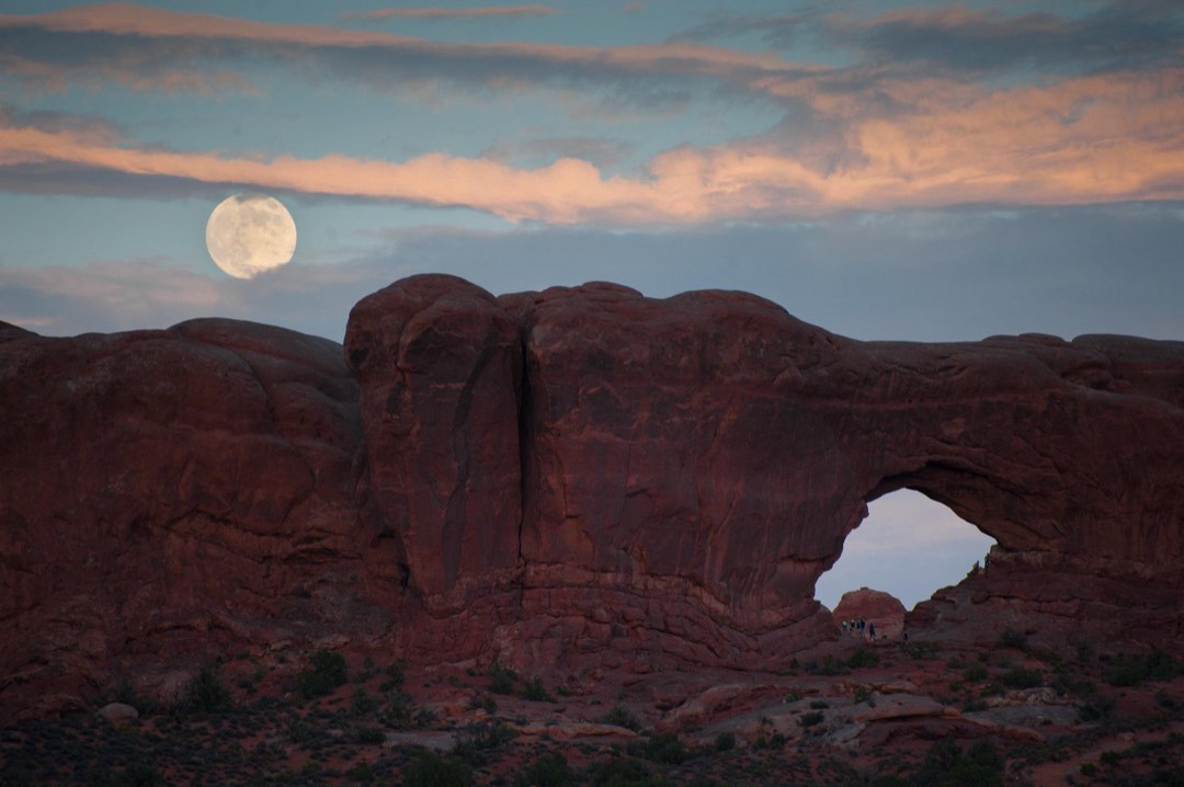 Large sandstone arch at dusk with a large white moon and clouds above