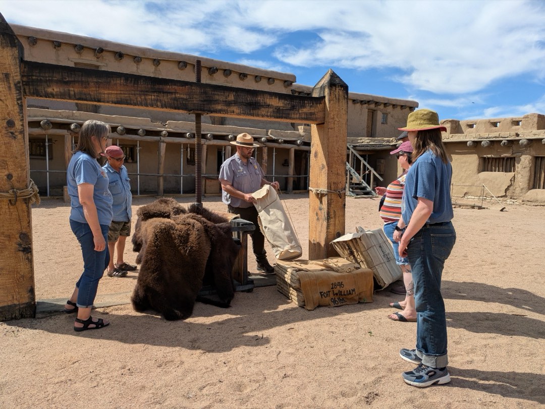 A group of visitors stand around a large wooden apparatus in a plaza courtyard.