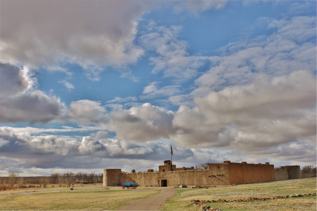 Bent's Old Fort with shortgrass prairie in foreground and blue sky and clouds above