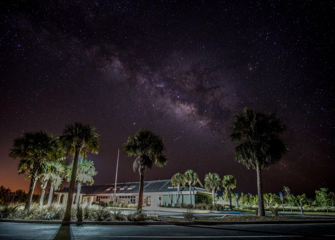 The milky way dominating a starry night sky over palm trees and a visitor center