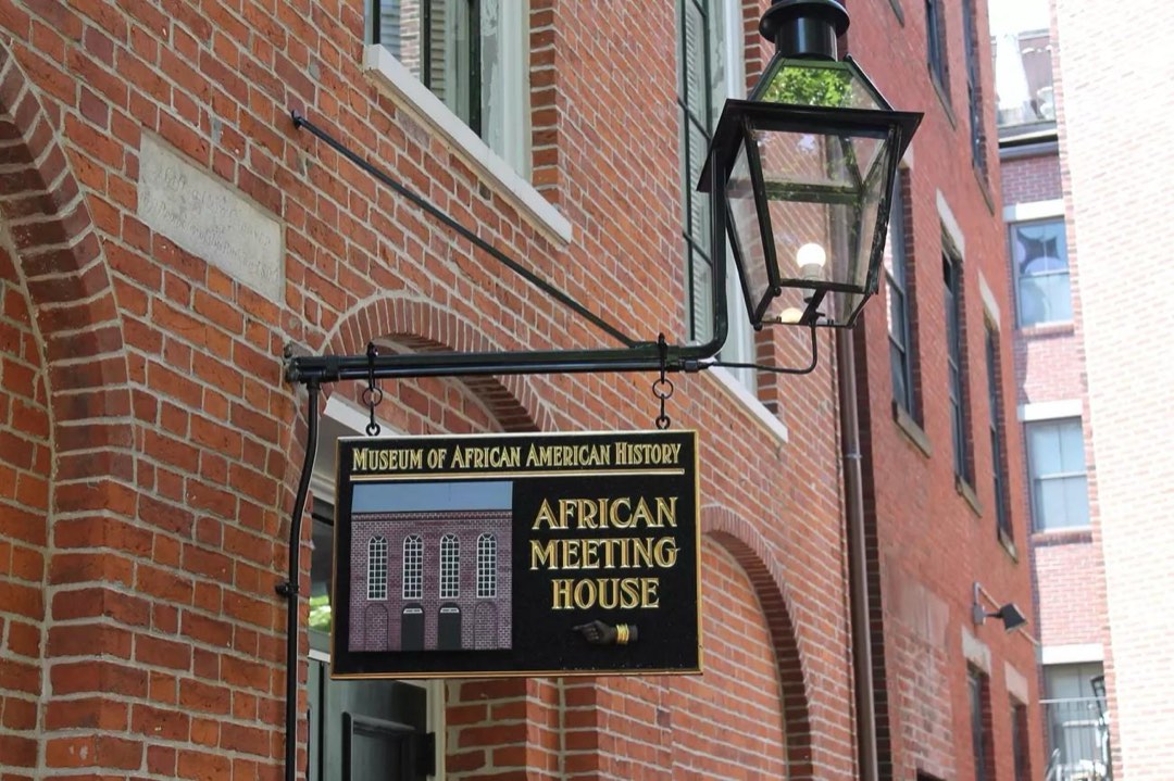 A sign hanging from a lightpost that is attached to a brick wall.
