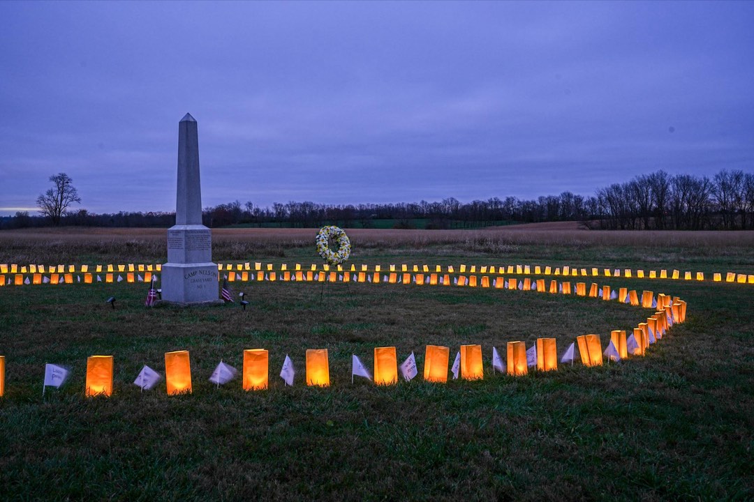 A stone obelisk in a grass field surrounded by luminary bags