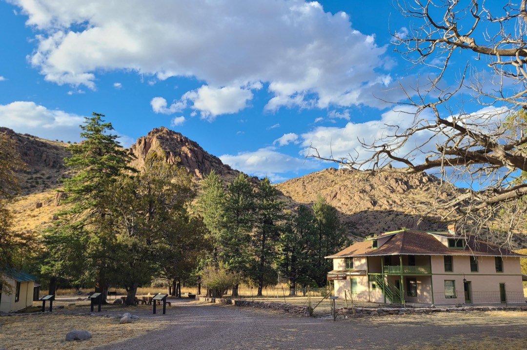 A ranch house in a green field surrounds by low mountains
