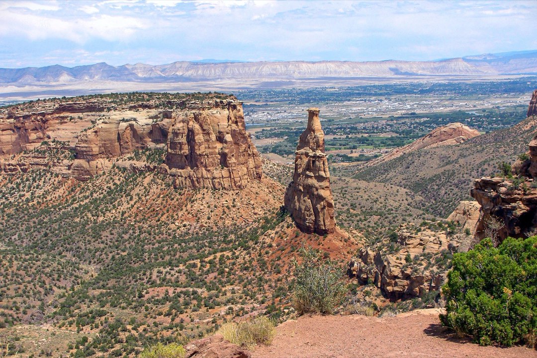 sandstone spire hundreds of feet tall stands above sparsely vegetated canyon bottom and cliffs