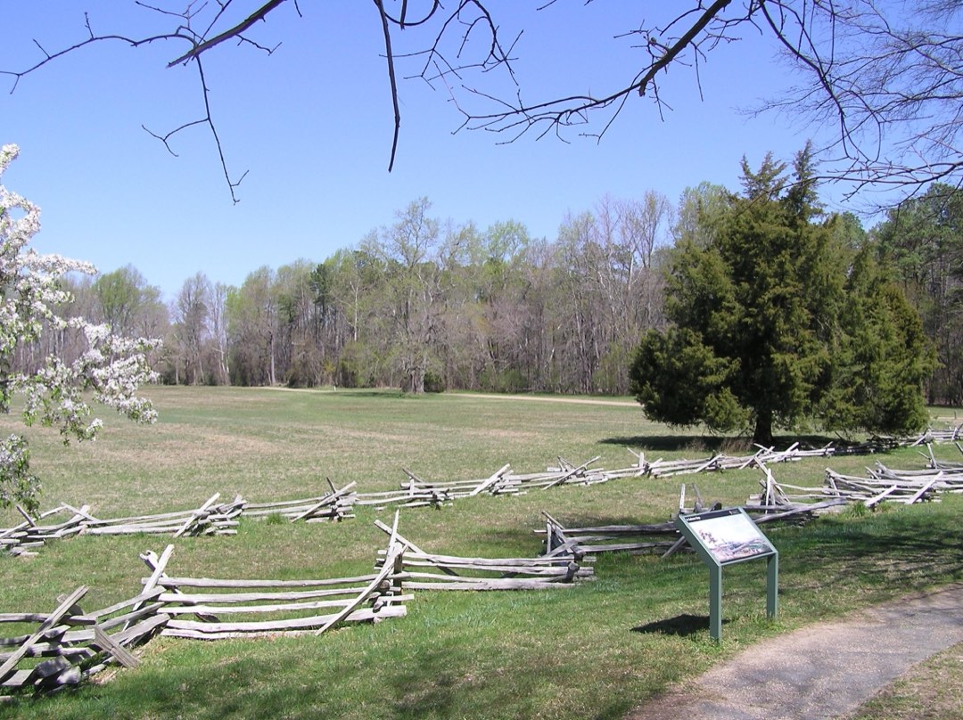 Wooden split rail fencing and flowering trees surround a grassy field behind an interpretive panel