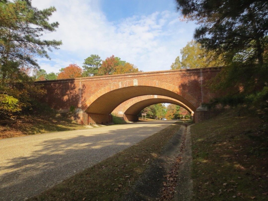 Two brick arch bridges span a wood shaded road