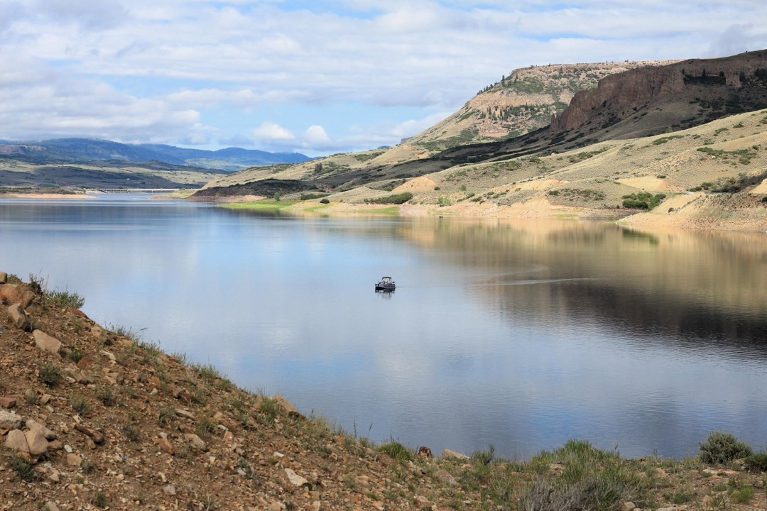 A single boat floating out in a reservoir. Mesas surrounding the area are reflected on the water.