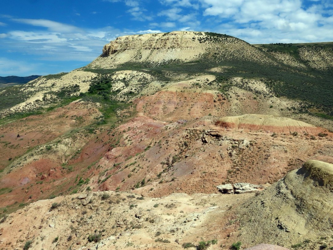 Hills with tan and red sediments partially covered with green vegetation.