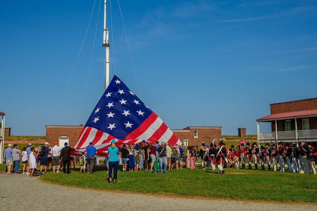 Visitors hold the edges of a large American flag as it is raised on to a large flagpole