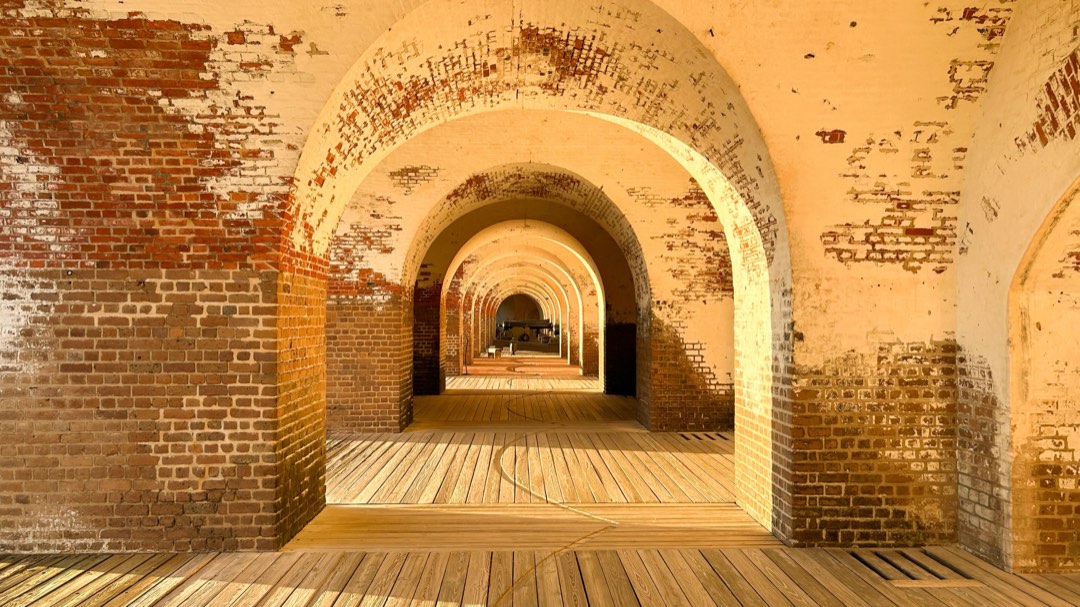 The brick of the fort glow in the late afternoon light. The arches inside the fort reveal a cannon i