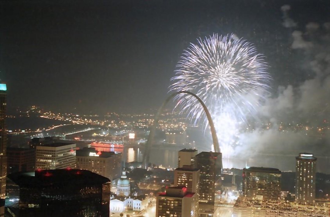 fireworks in the sky over the Arch and city buildings with the river in the background
