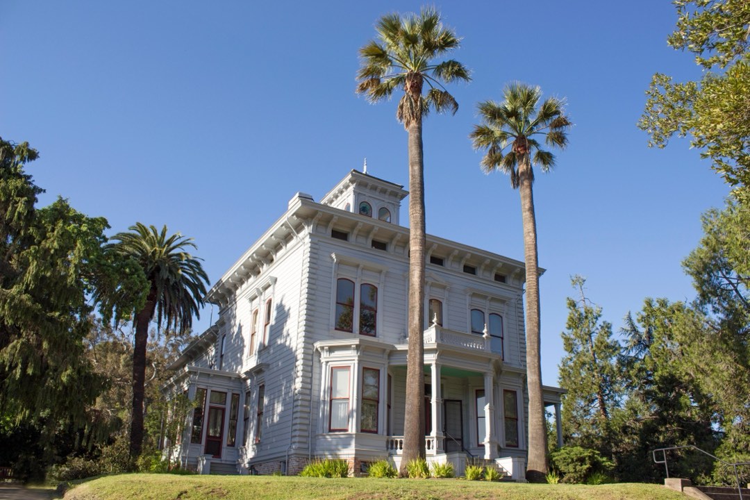 White two story house capped by a bell tower and ringed with palm trees