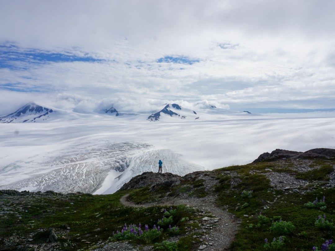 A person looks out over a view of snow, ice, and mountain peaks