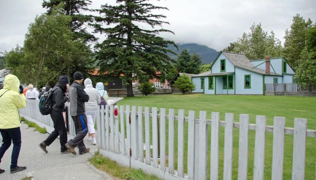 A pale blue building with green trim sits in front of a tidy lawn with a white picket fence.